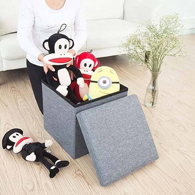 A grey ottoman being used to store toys