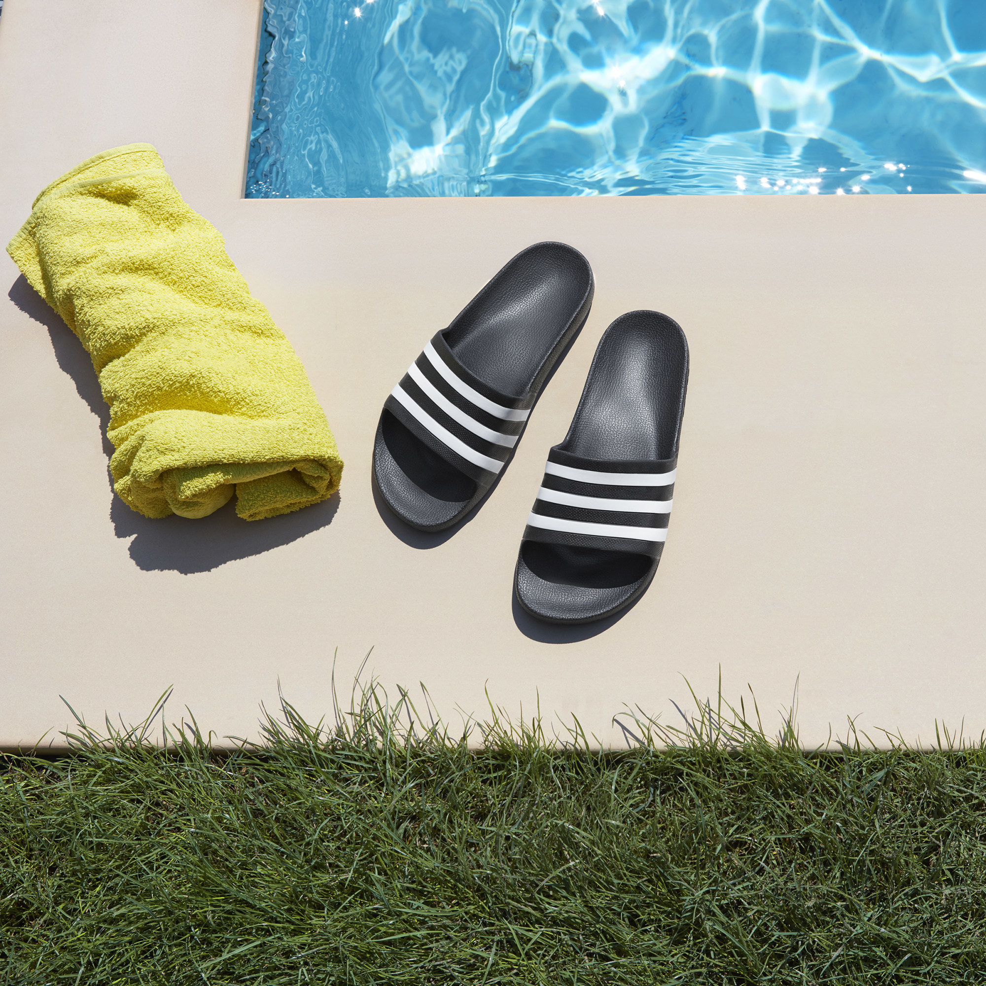 a pair of adidas aqua slides on the side of a pool beside a towel