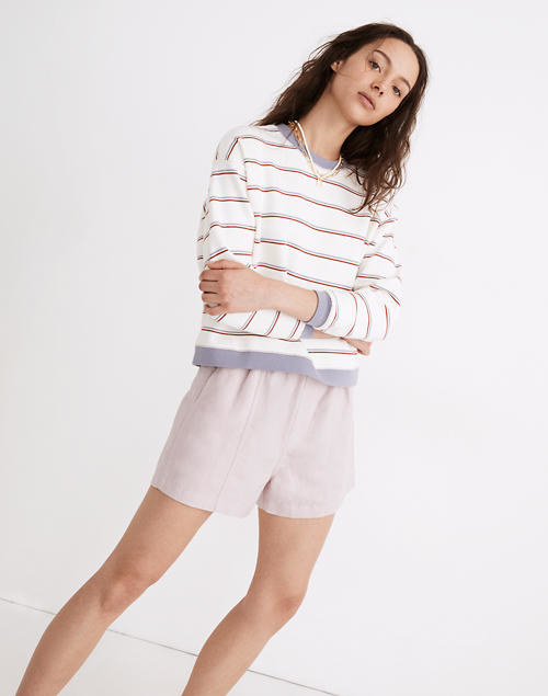 A model wears the white sweatshirt with gray and red stripes and gray cuffs