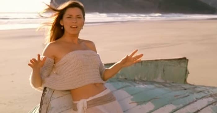shania twain in a crop top leaning on a boat on a beach