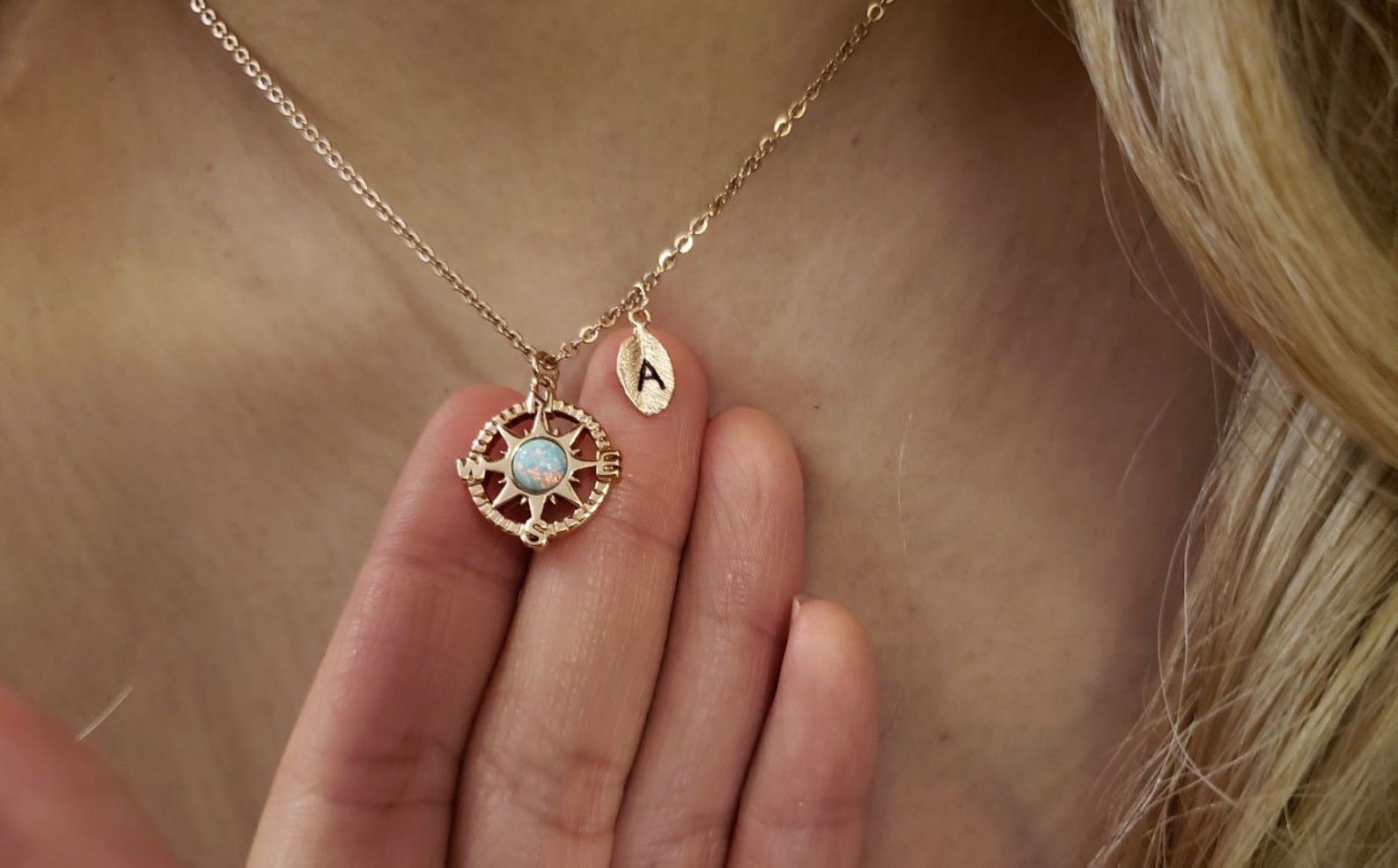 Model is wearing a necklace with a gold compass and leaf that has the letter A engraved