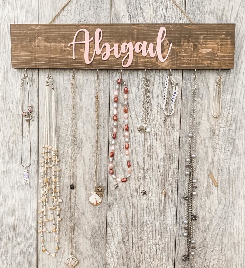 The wood hanger with various necklaces hanging from it and the name Abigail on it in pink