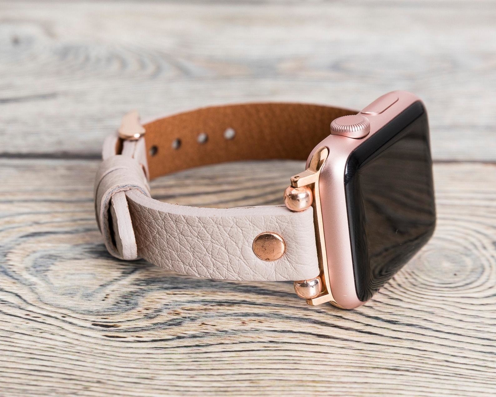 An Apple watch with a pink leather band and rose gold accents
