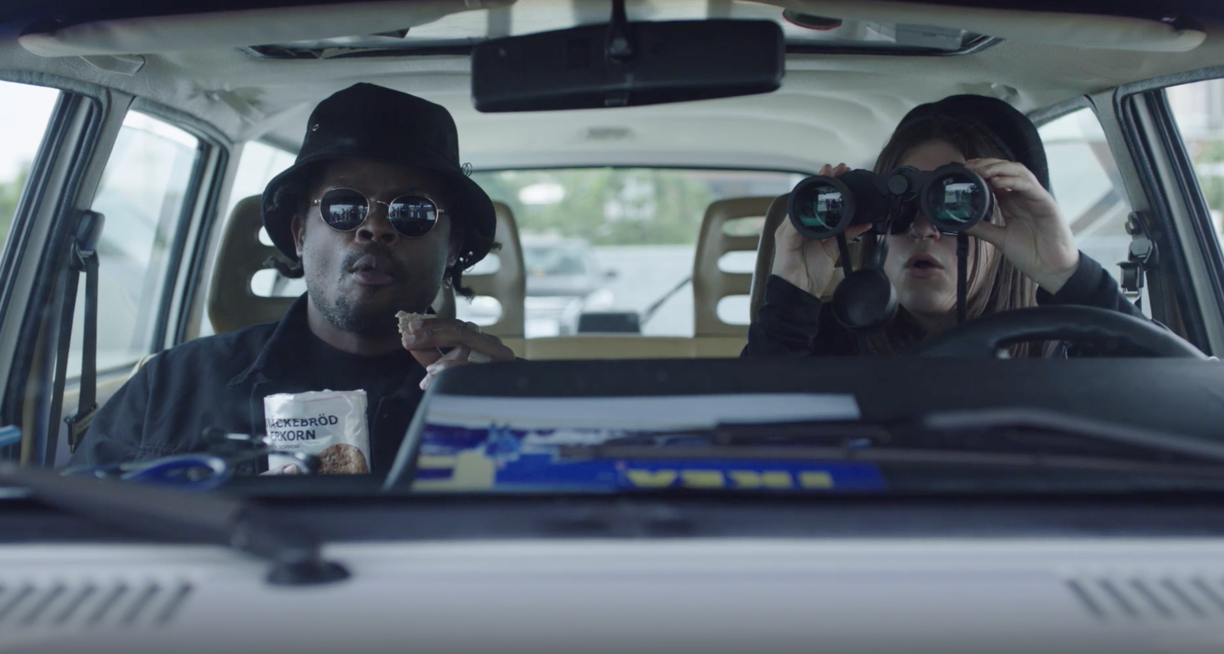 Two people sitting in their car in a stakeout.