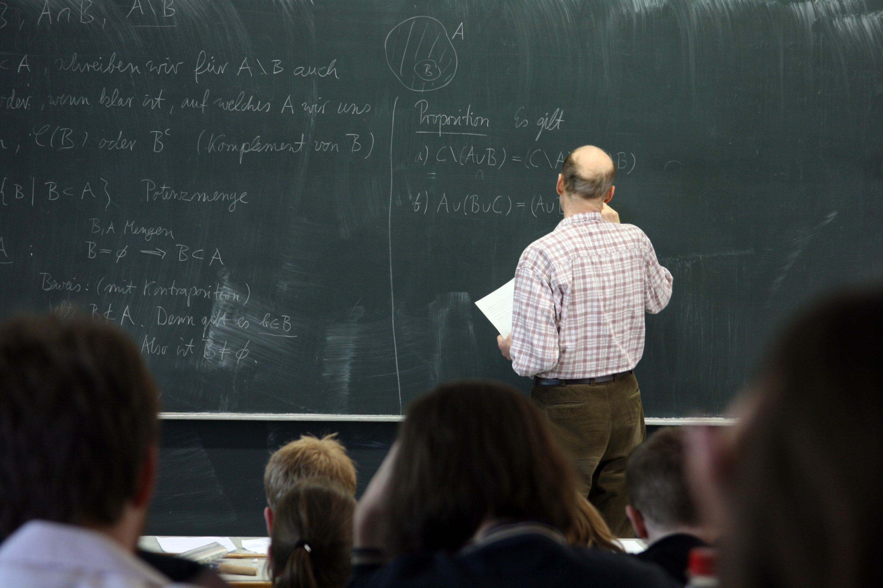 A professor writing on a chalkboard with his class watching