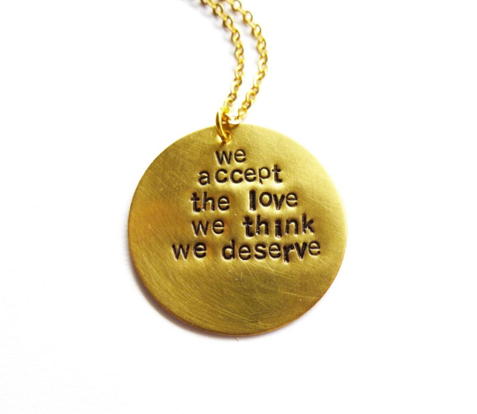 gold circular pendant with the words &quot;we accept the love we think we deserve&quot; on it