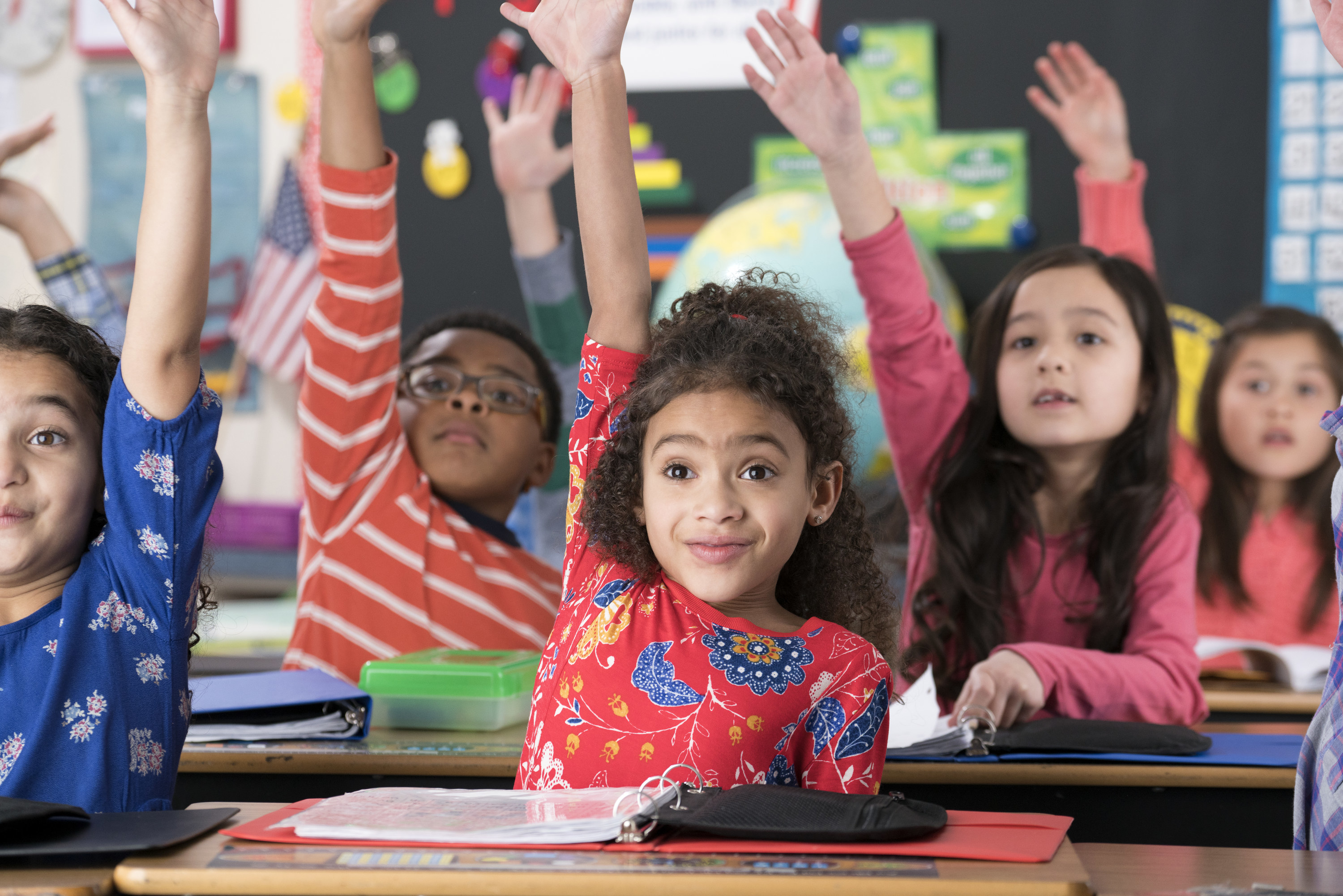 Young students eagerly raise their hands high in a classroom