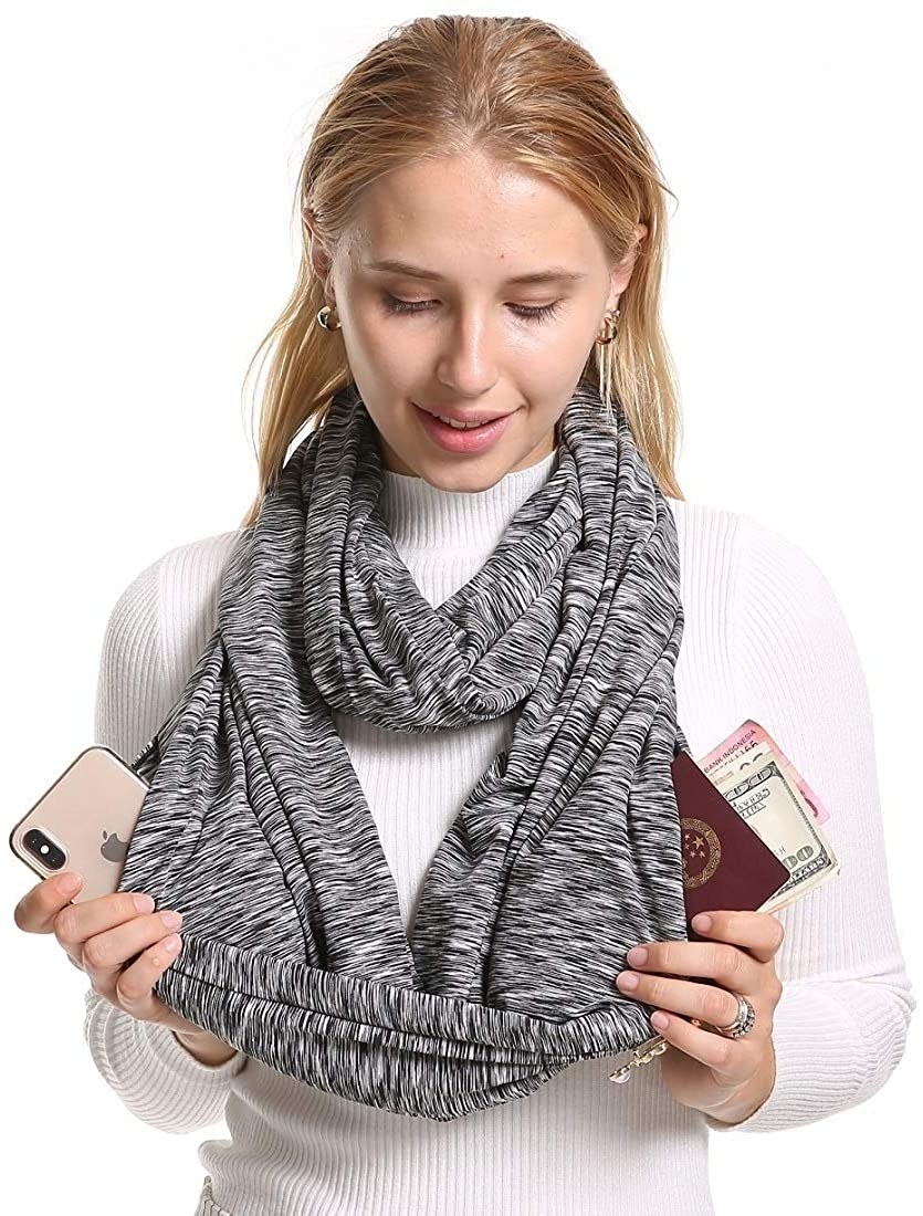 model wearing the scarf and showing her phone, passport, and money can fit in the scarf