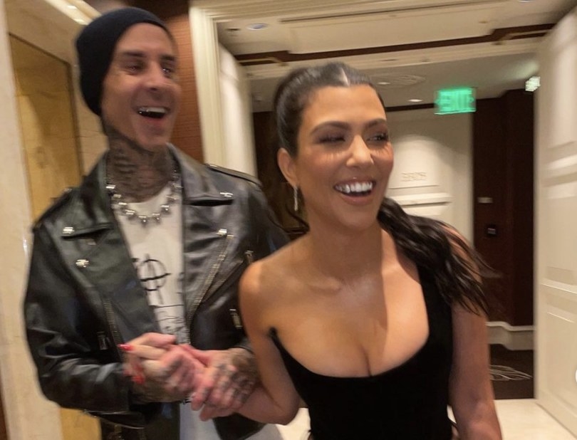 Kourtney smiles while Travis holds her hand while walking down a hallway