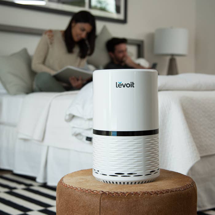 white cylindrical air purifier sitting on an ottoman in a bedroom