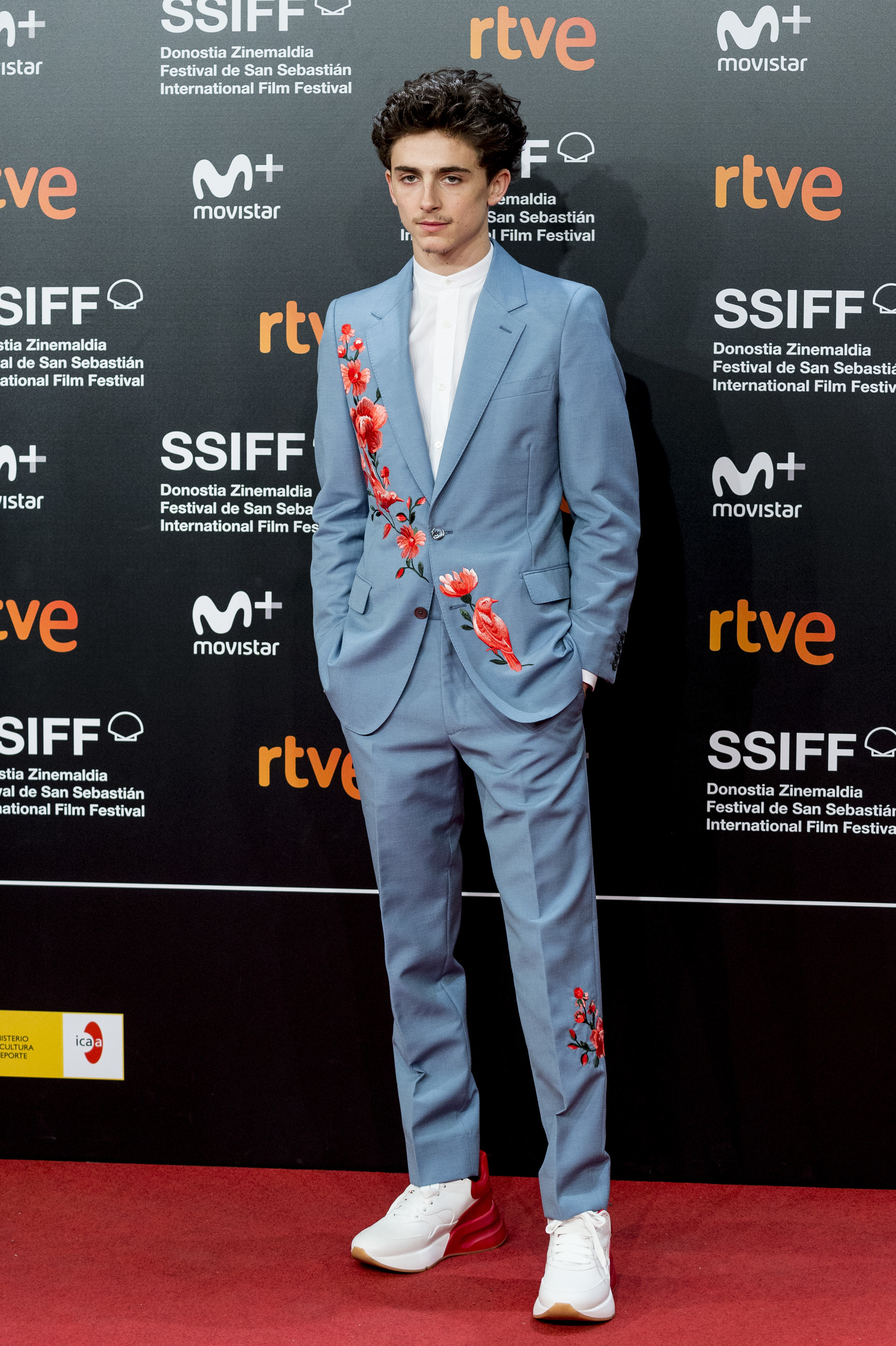 Timothée wears a light blue suit with embroidered red flowers across the chest
