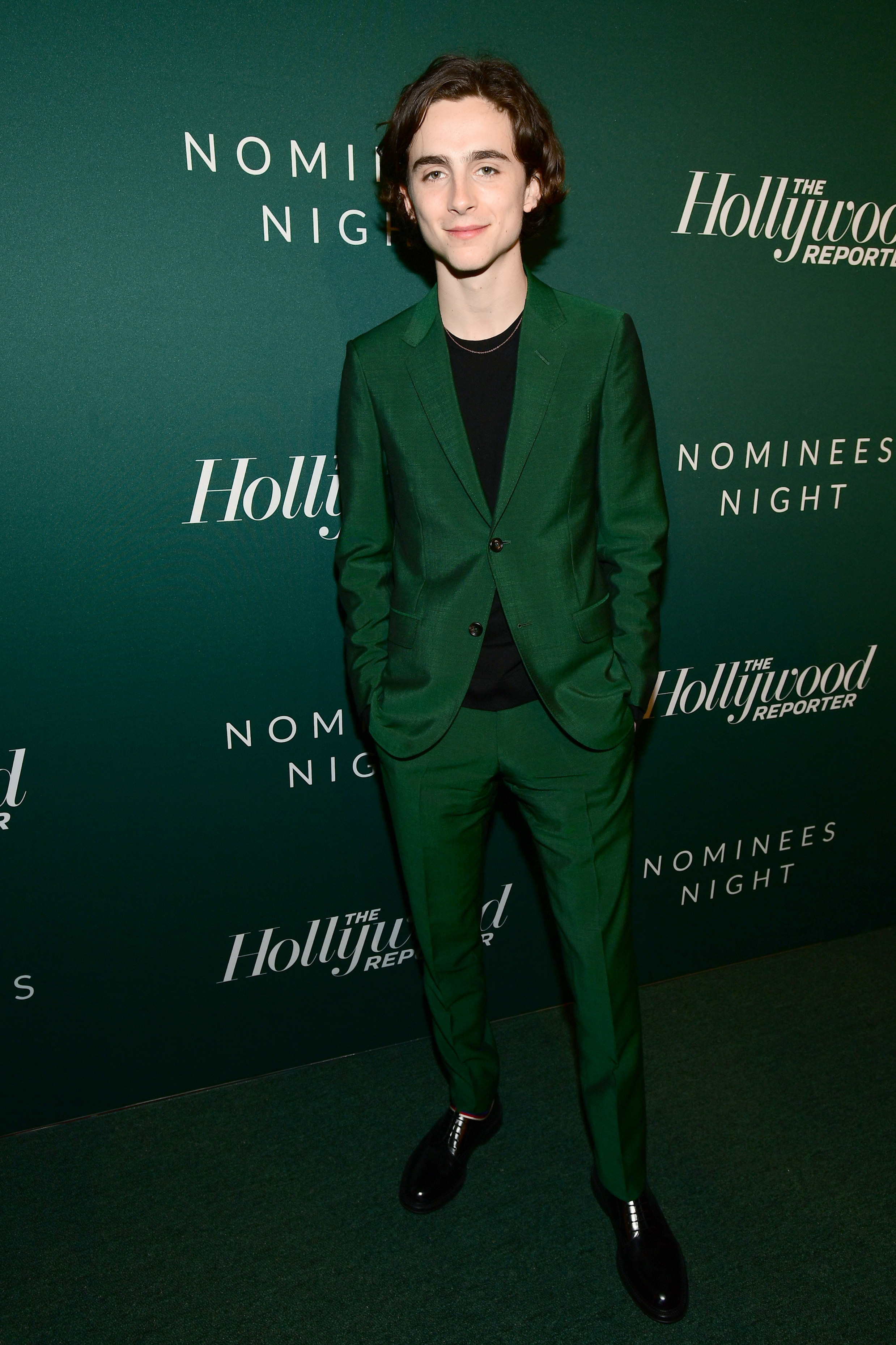 Timothée wears a forest green suit in front of the same color backdrop and carpet