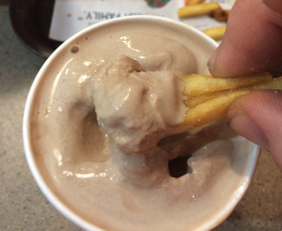 A hand dipping hot chips into a chocolate thickshake