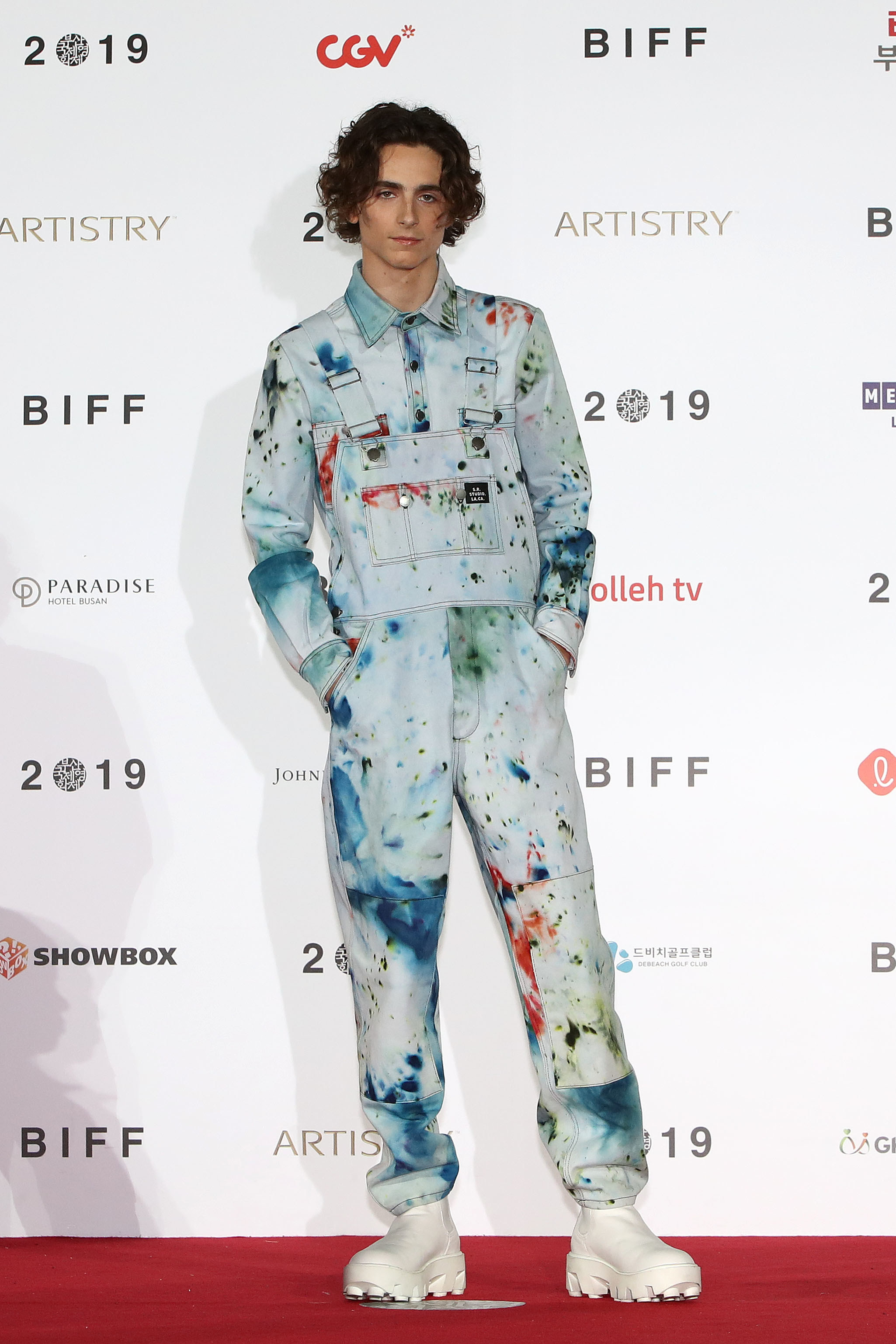 Timothée wears splatter-painted overalls with a matching long sleeve button down