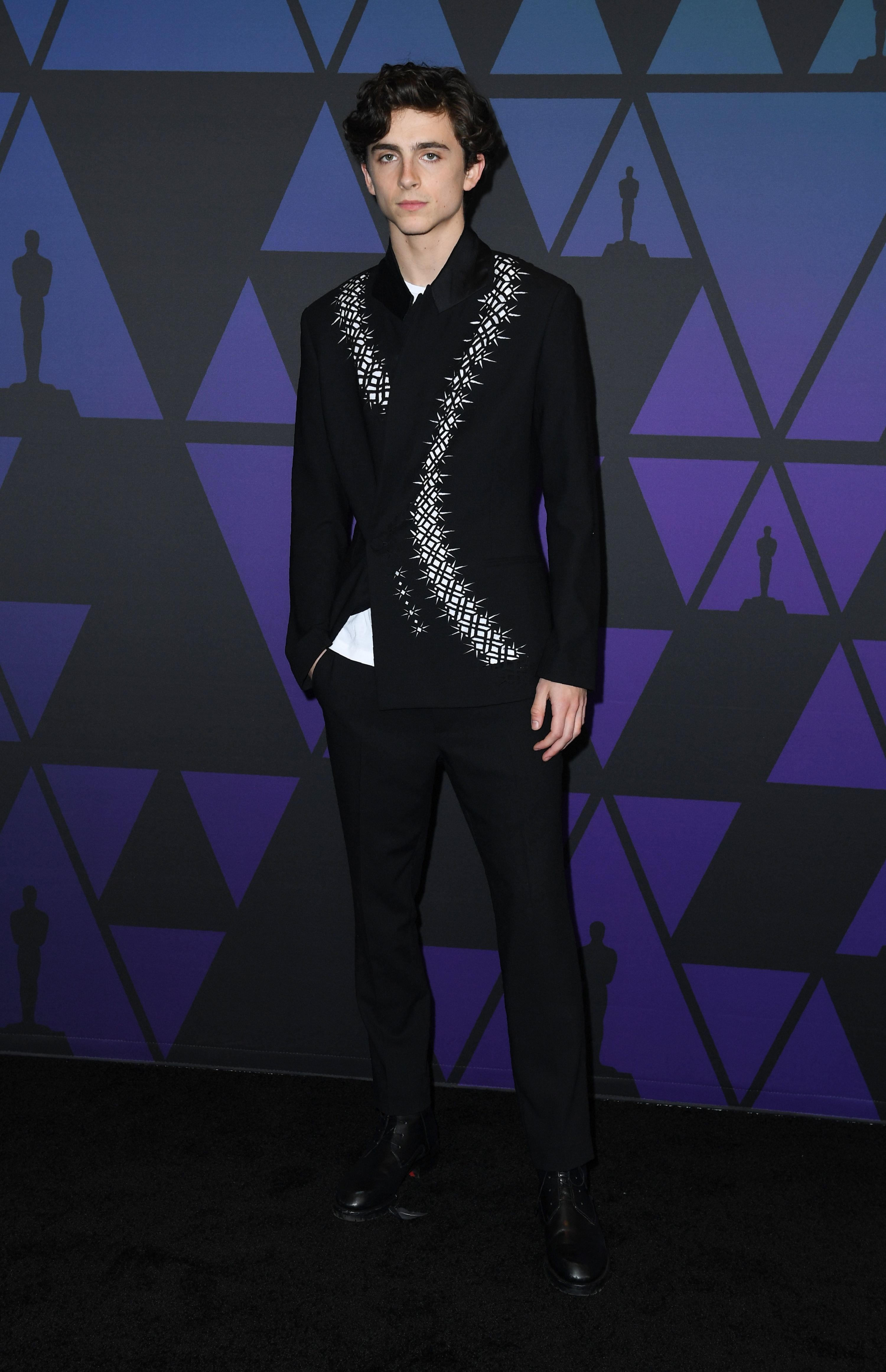 Timothée wears a black suit with a print of a white snake that wraps around the neck