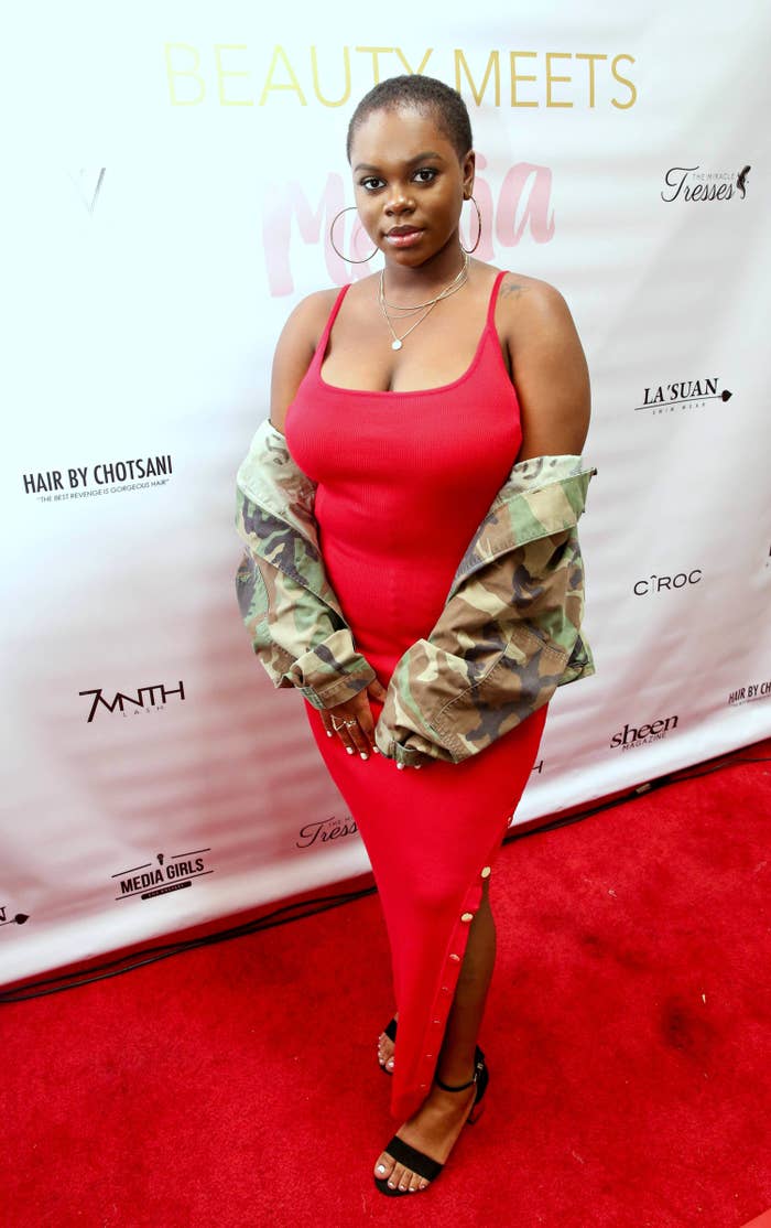 Cori posing on a red carpet in spaghetti strap dress and an army fatigue printed jacket