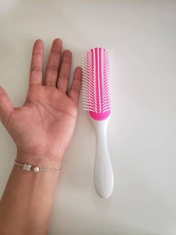 A customer review photo of their hand next to white brush on table to show the size