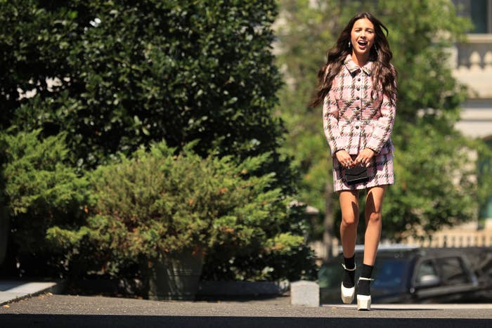 Olivia Rodrigo wearing a plaid dress and jacket walks to the White House