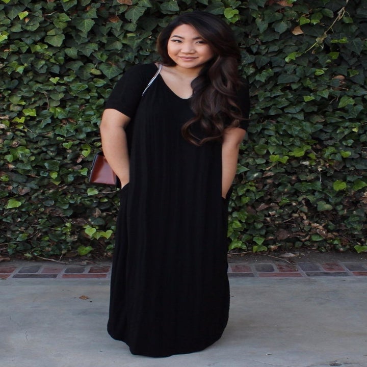 a reviewer wearing the short sleeve black maxi dress with their hands in the pockets 