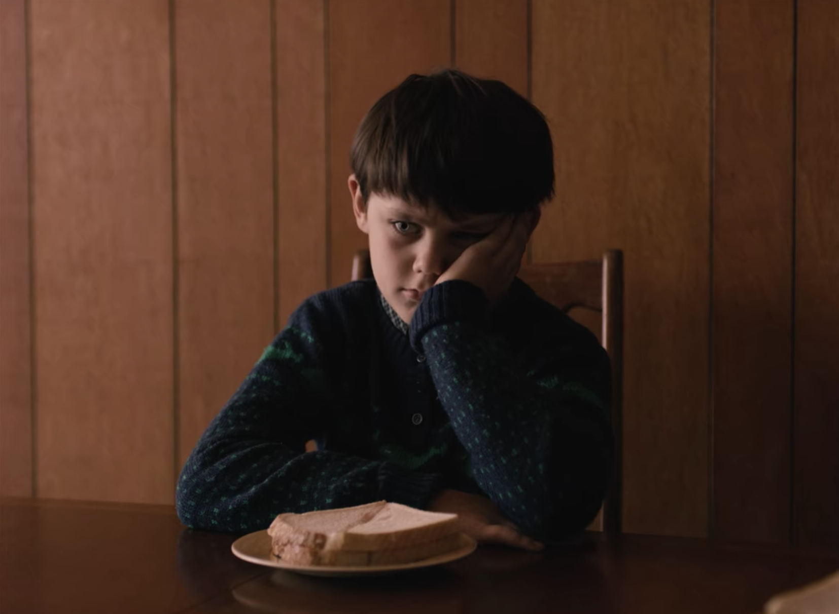 Jack sitting at a table in front of a sandwich with his head in his hand