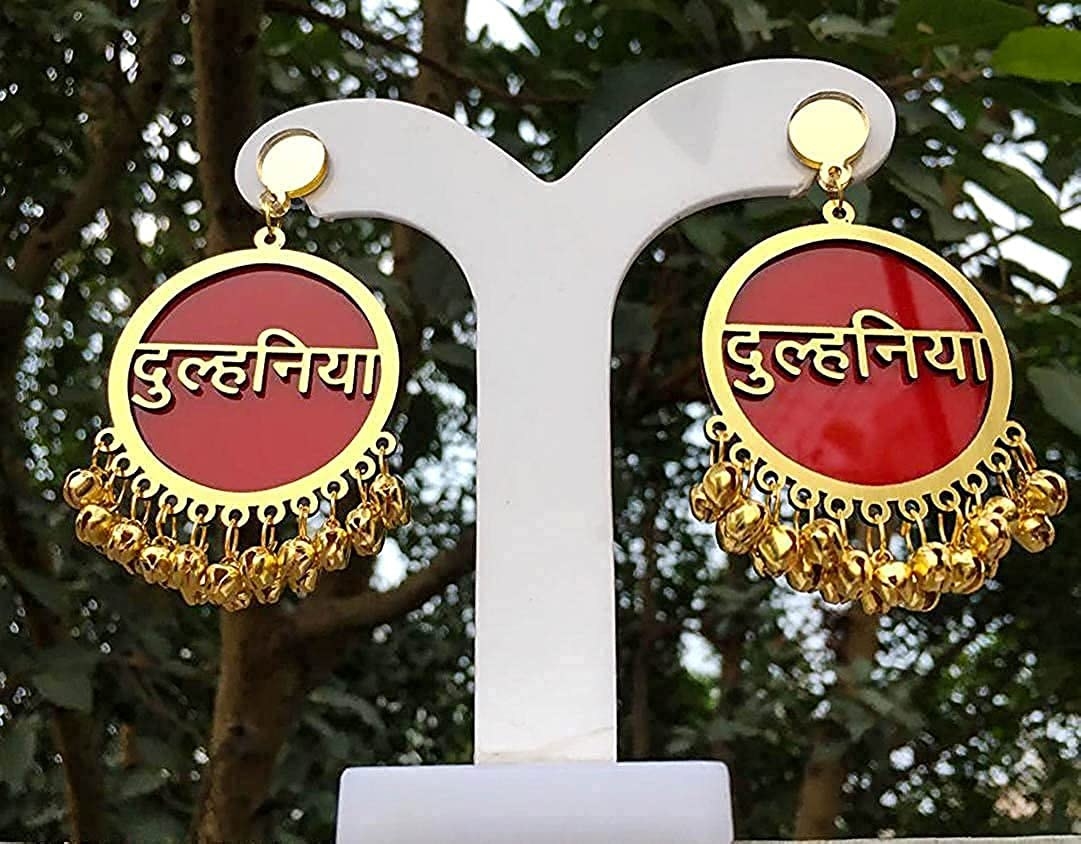 A pair of red and gold jhumkas with the words &#x27;Dulhaniya&#x27; written on them in Hindi