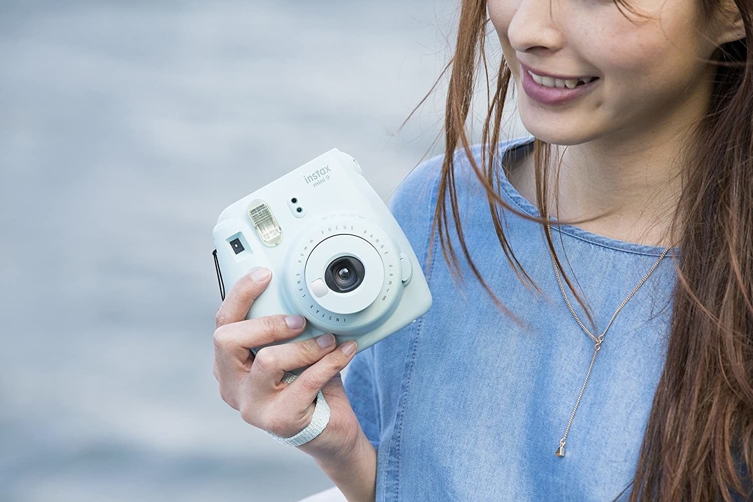 A woman holding a blue Instax mini instant camera in sky blue shade