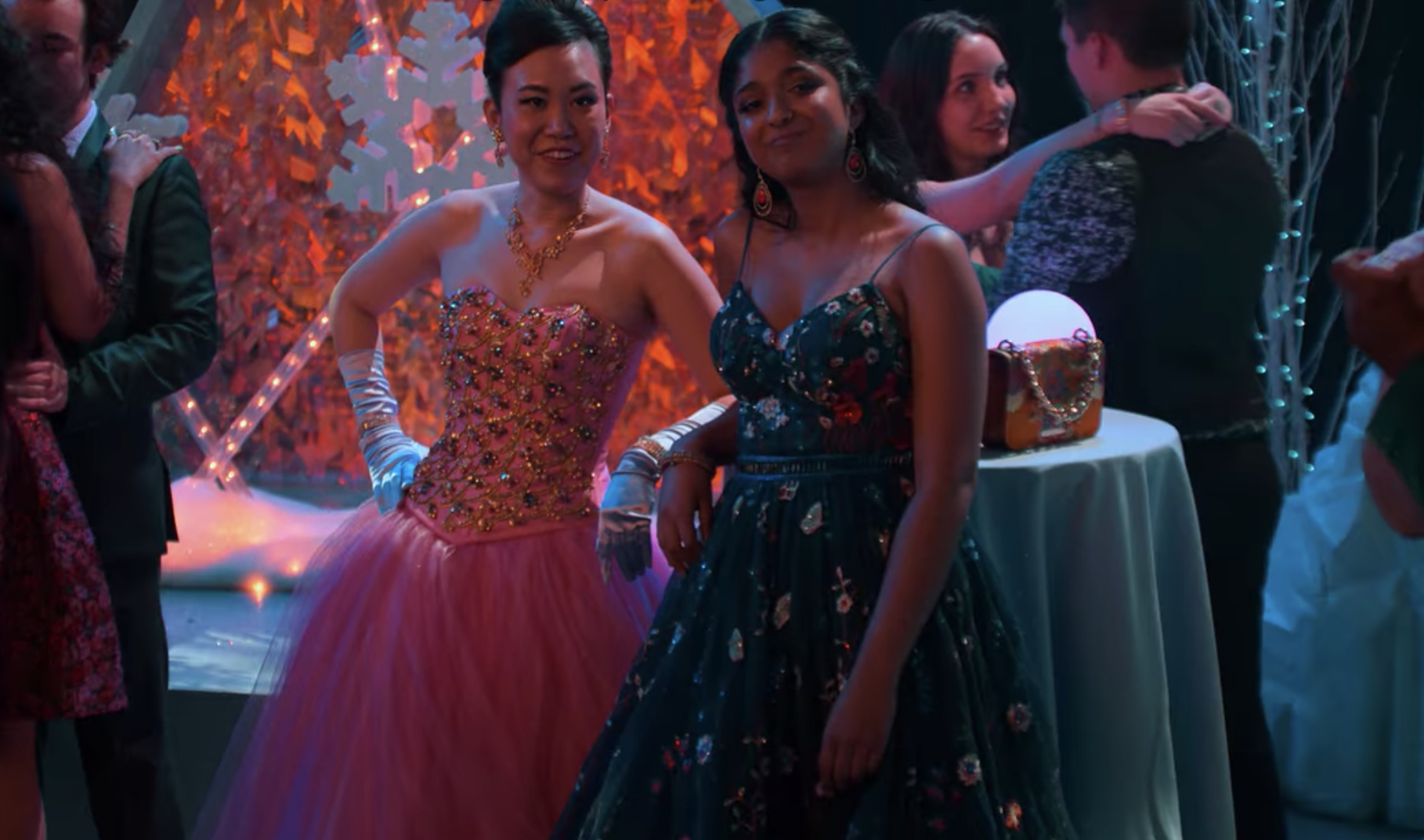 Eleanor and Devi are standing dressed in formal gowns at their school dance