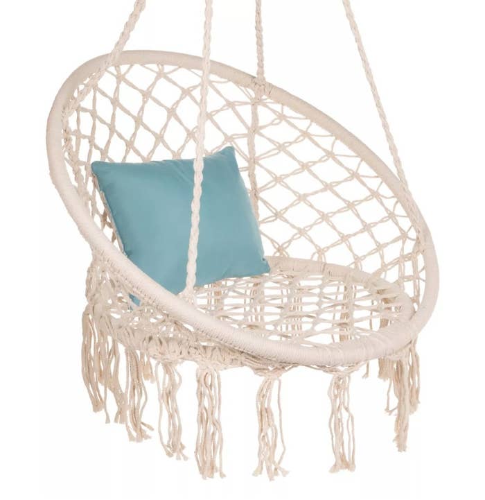 A beige, macramé hammock with tassels and a blue pillow atop