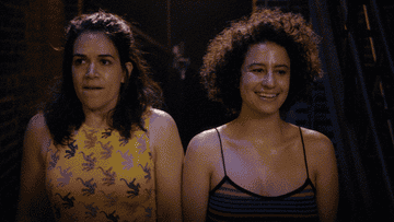 A close up of Abbi and Ilana standing next to each other as Ilana says, &quot;God, I&#x27;m feeling something, you know? It&#x27;s upon us&quot;