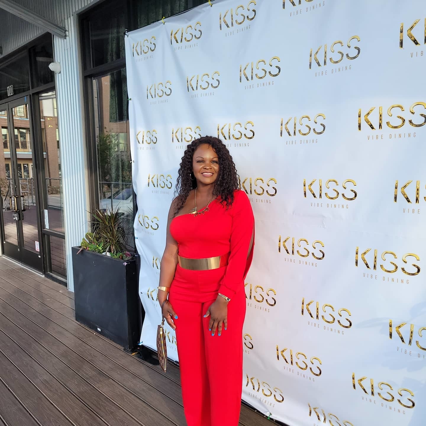 image of reviewer wearing the red one shoulder jumpsuit in front of a step-and-repeat