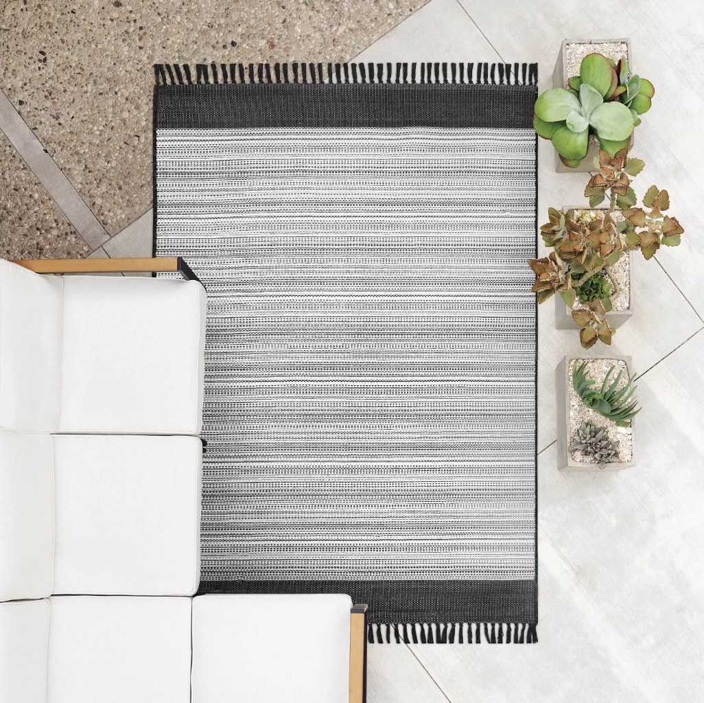 A black/white, striped, fringe outdoor area rug displayed on a patio