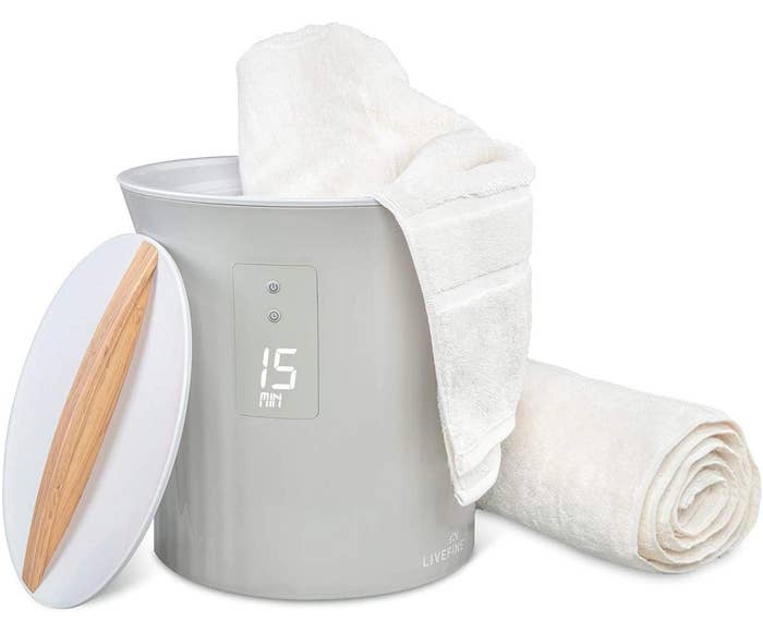 a gray towel warming machine with white lid and bamboo handle next to white towels