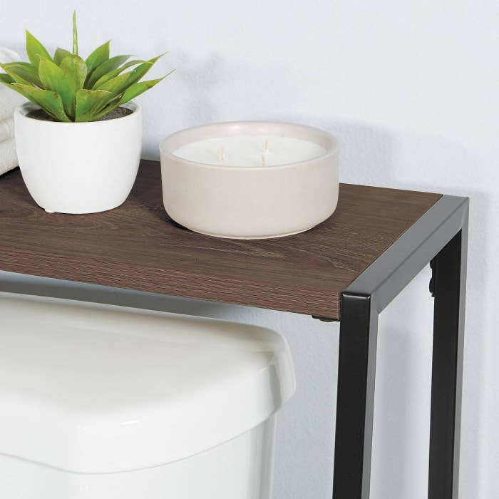 an over-the-toilet shelf with a candle and plant on top