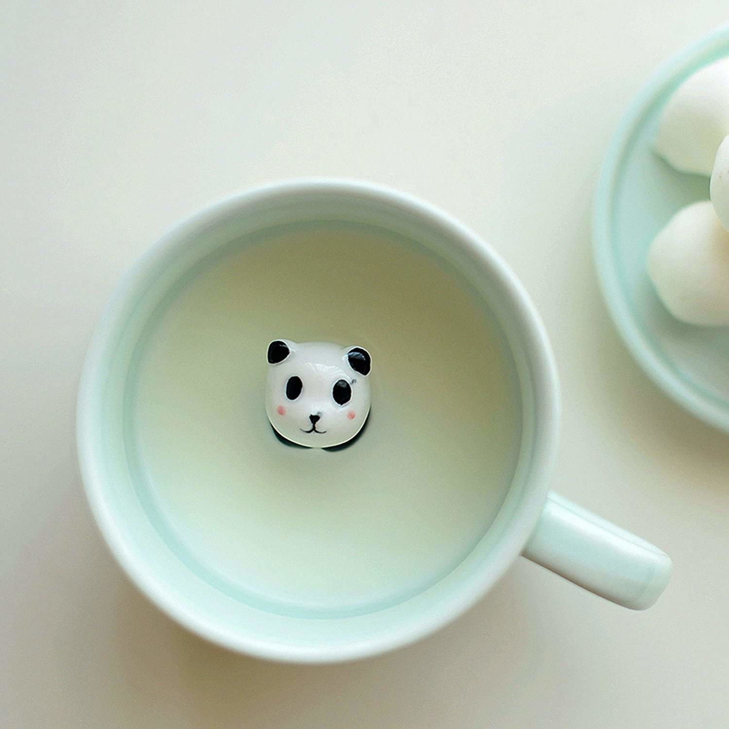 A mug with some milk in it and a panda looking up from it