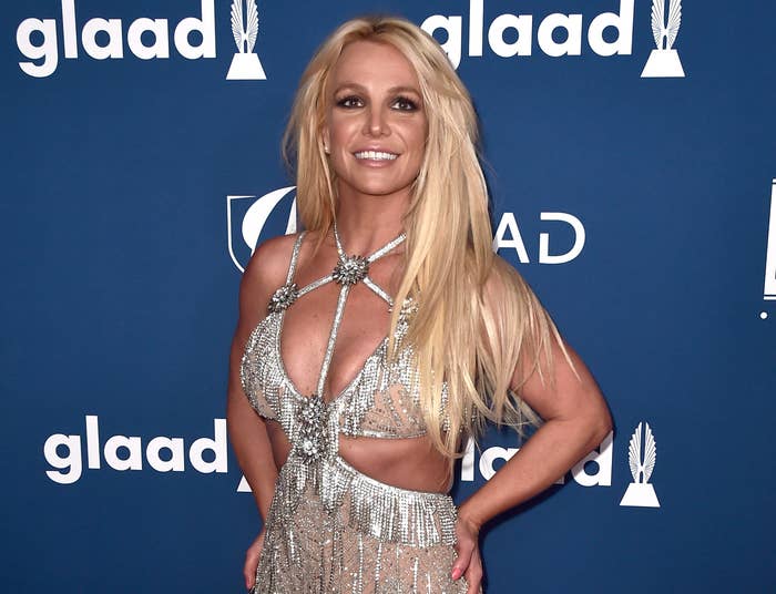 Britney poses with her hand on her hips and smiles