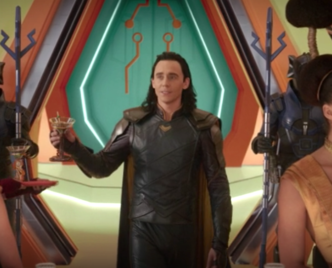 Loki holding a martini glass, wearing his blue and yellow outfit in Ragnarok