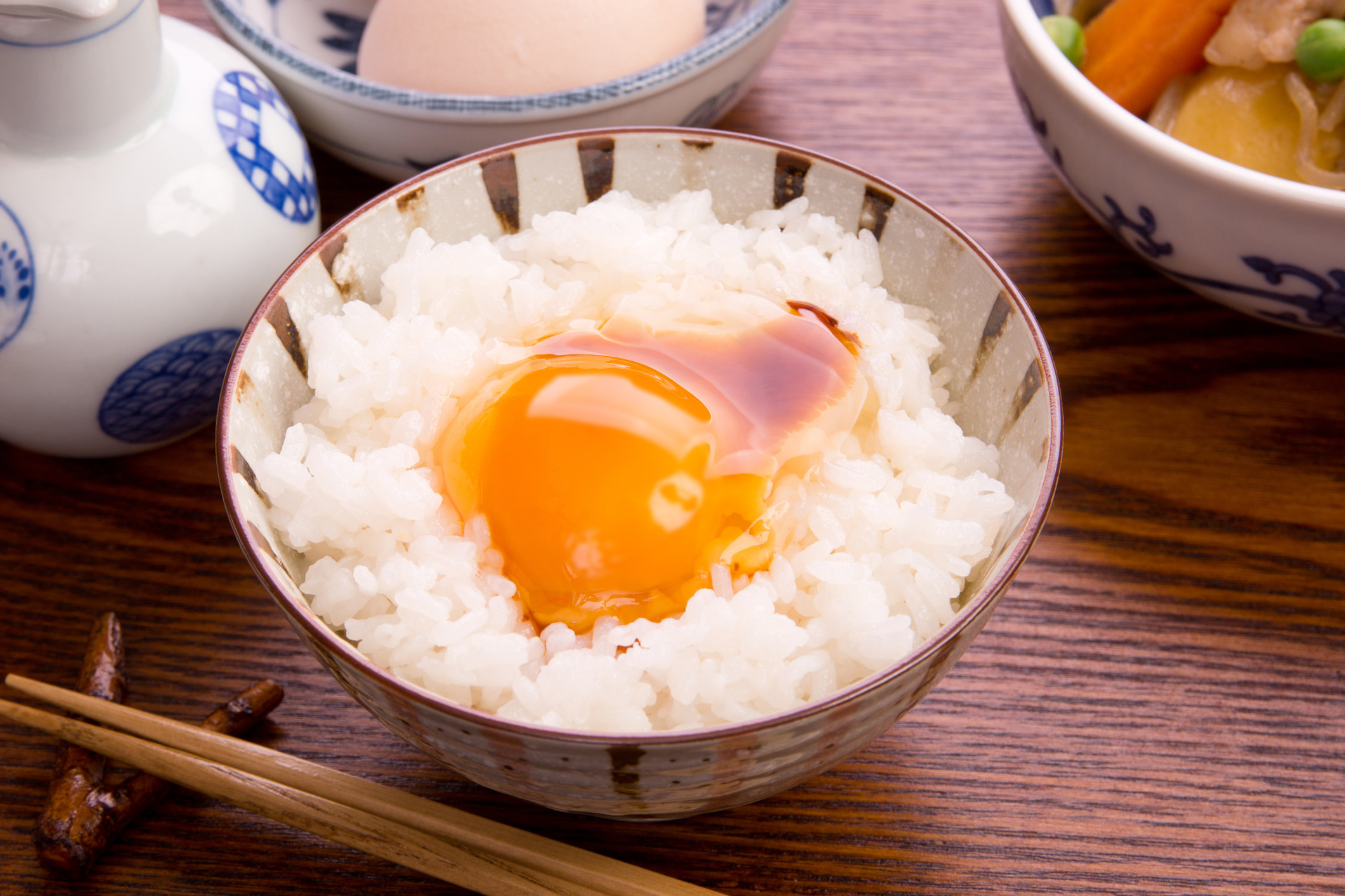 A raw egg on top of white rice topped with soy sauce in a small bowl