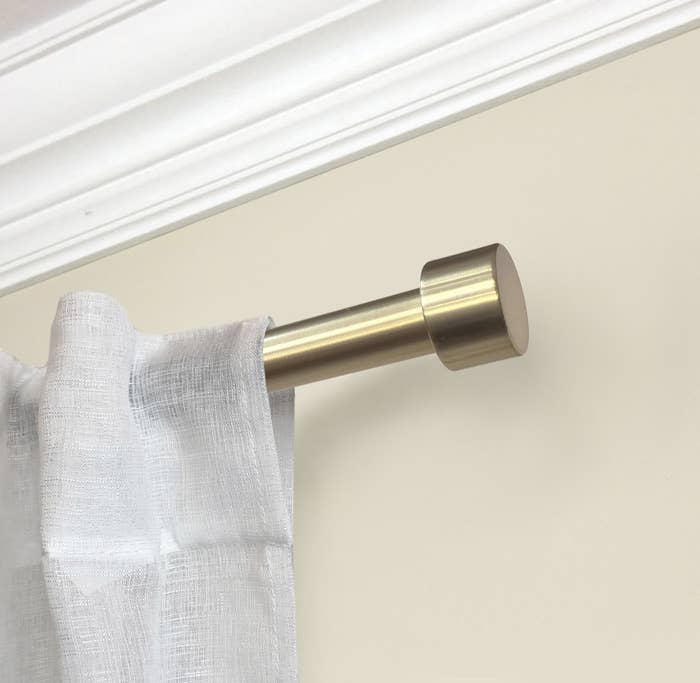 The gold rod has a cylindrical end and is holding up a white linen curtain