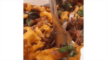 A close up shot shows a fork digging into loaded fries with cheddar, onion, pulled pork, parsley and fries.