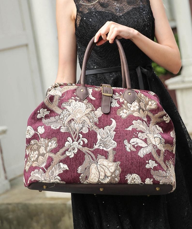 Model is holding a red Victorian-style bag with a beige floral pattern on it