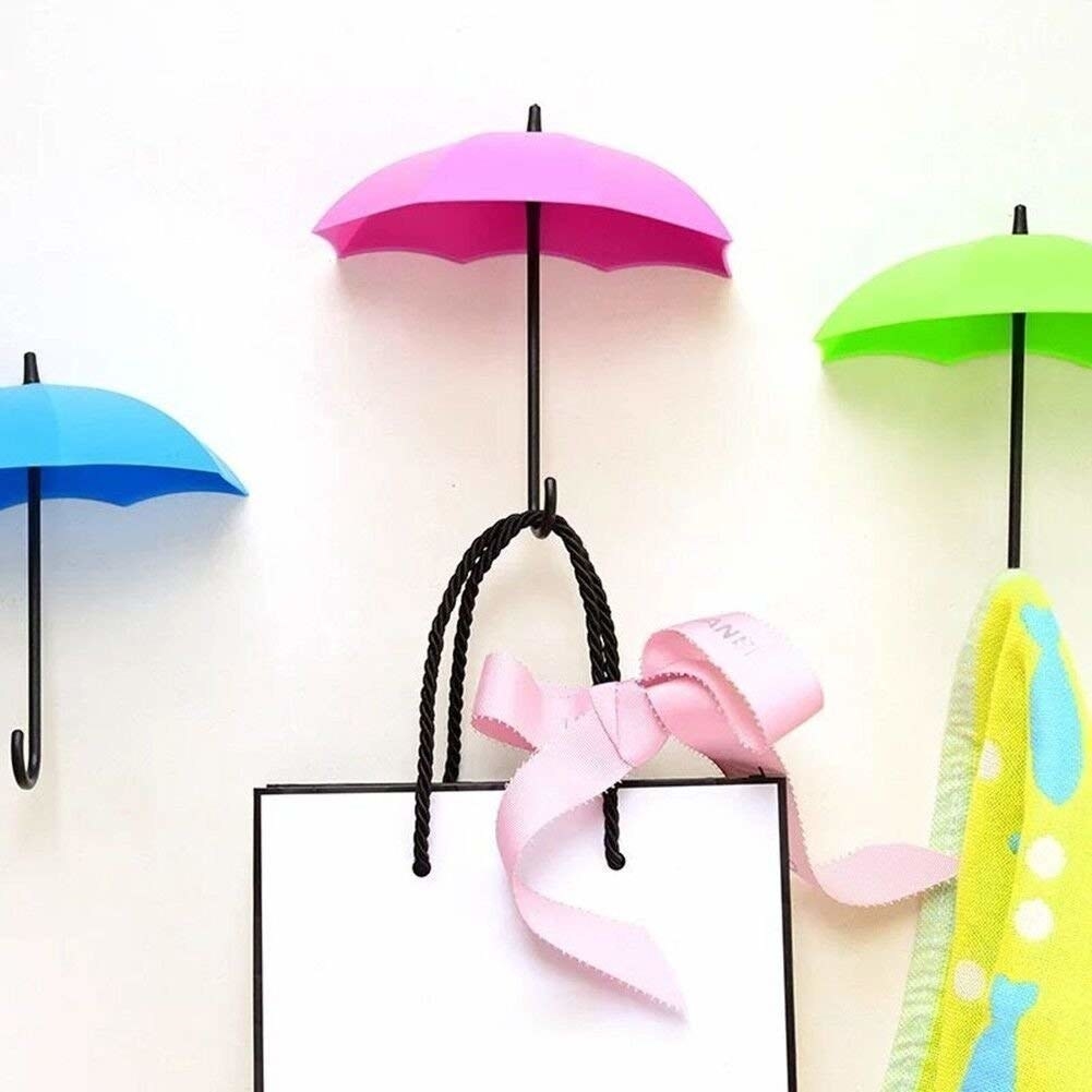 Blue, pink, and green umbrella-shaped wall hooks holding up a napkin and a small shopping bag
