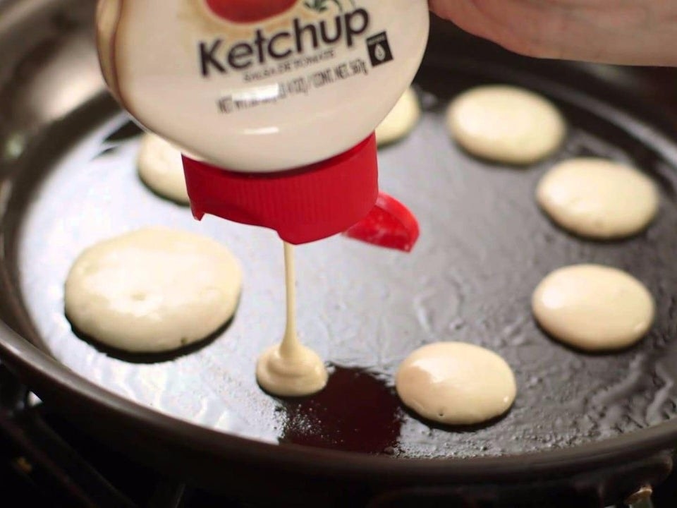 Pouring pancake batter onto a skillet from an empty ketchup bottle.