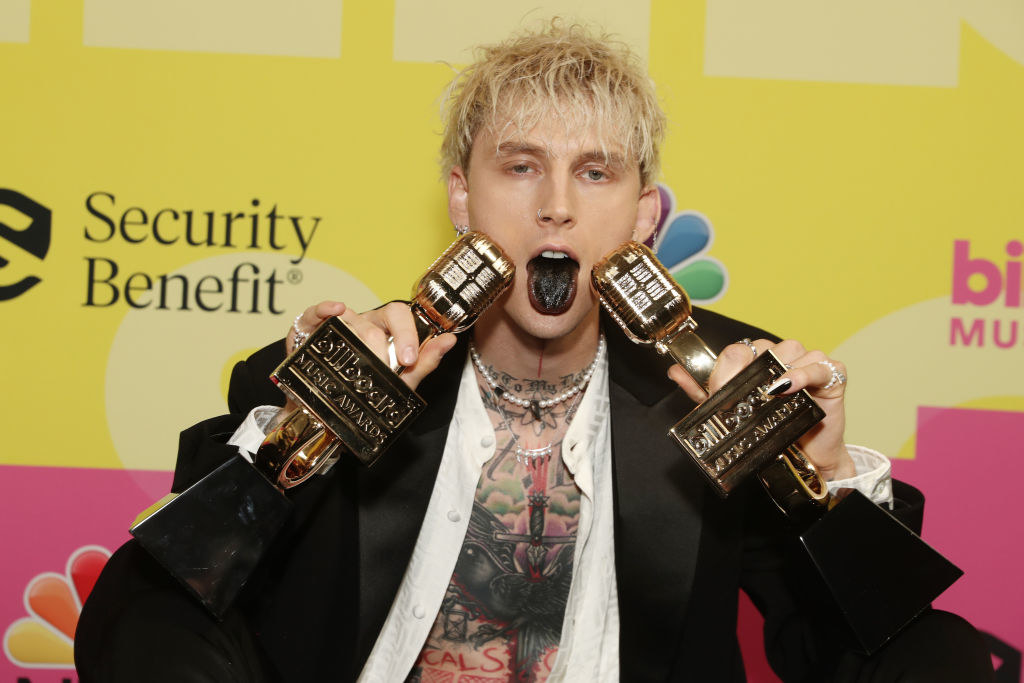 MGK holding up his two BillBoard Awards and sticking his tongue, which is dyed black, out