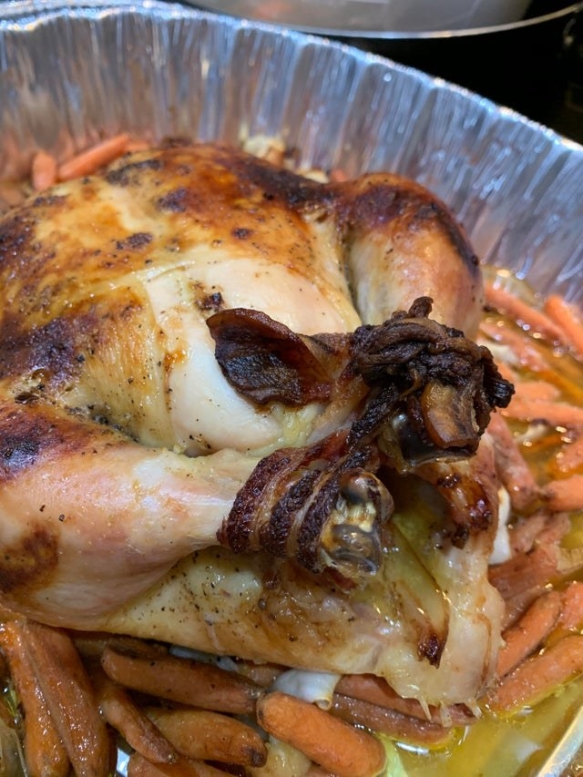 A whole chicken with its legs tied together by bacon.