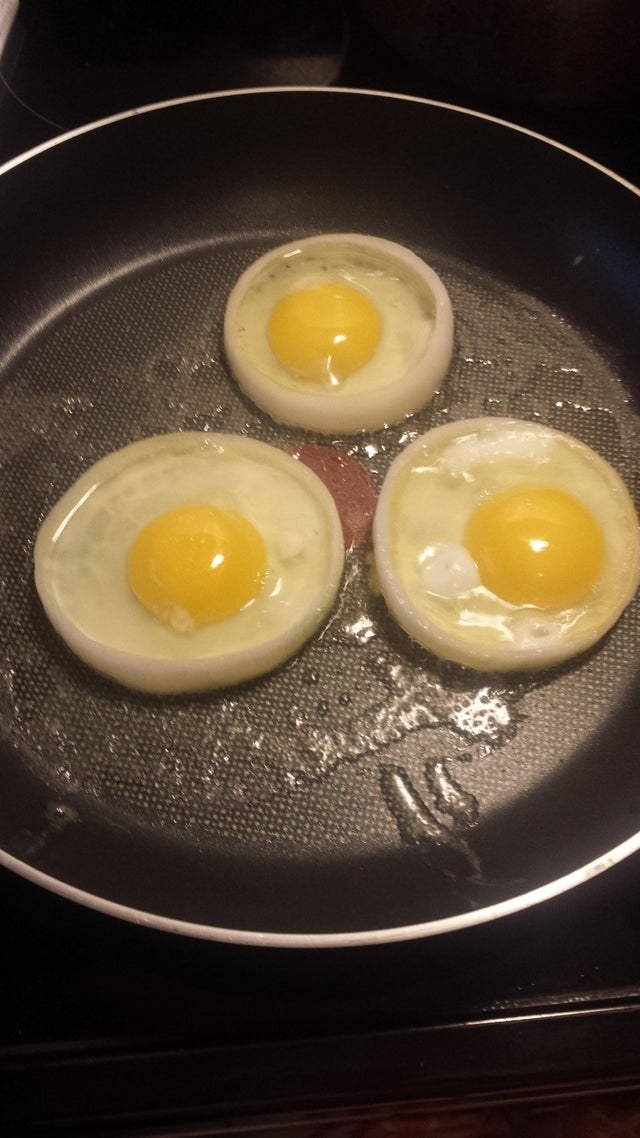 Three eggs cooking inside of onion rings.