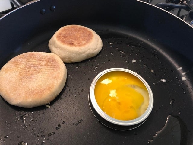 An english muffin toasting and egg coking inside a mason jar lid.