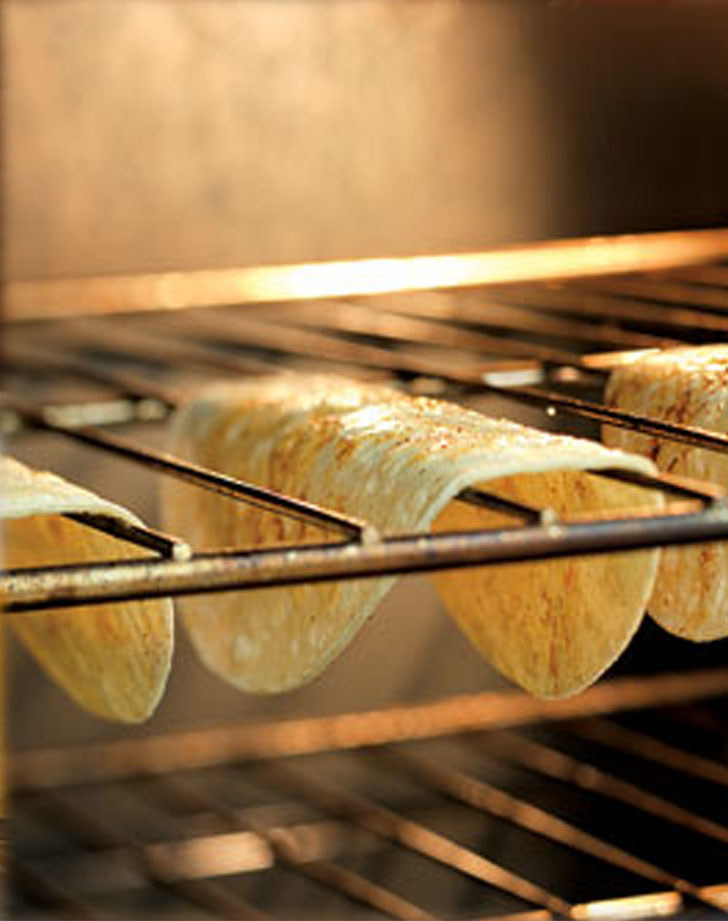 Tortillas crisping up by hanging on an oven rack.