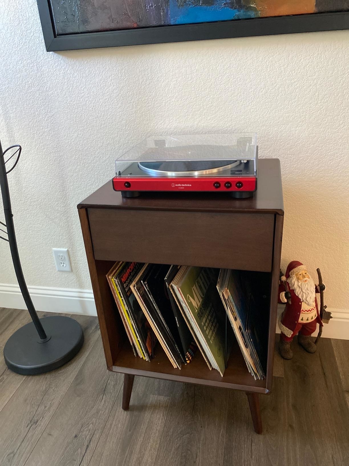 reviewer image of the black and red Audio-Technica record player on a small wooden table with record storage