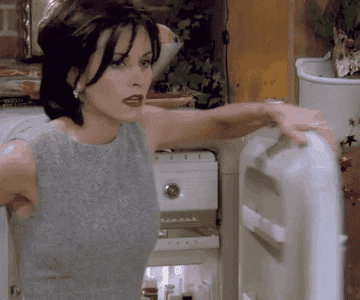 Monica cooling off by opening the fridge door
