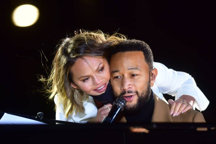 Chrissy leaning over her husband while he sings at the piano